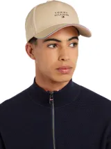 Gorra de béisbol color beige con visera ribeteada con cinta tricolor (rojo, blanco, azul). Presenta el logo de Tommy Hilfiger bordado en el frente.