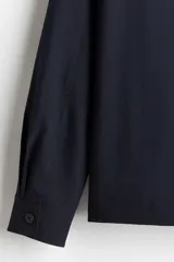 Sobrecamisa azul marino de corte recto, con cuello inglés, cierre frontal con botones, mangas largas con puños abotonados, dos bolsillos de parche en el pecho y canesú en la espalda.