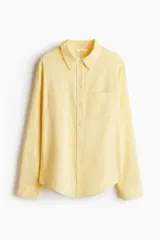 Camisa amarilla de tejido liviano de mezcla de lino y viscosa con cuello, botones adelante y canesú de doble capa con pliegue de caja en la espalda. Modelo de manga larga con bolsillo superior abierto, puños abotonados y bajo redondeado.