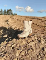Bota corta de cuero color marrón, con taco de madera y punta cuadrada. Presenta una correa con hebilla alrededor del tobillo.