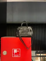 Cartera negra de simil cuero con correa corta y correa larga ajustable. Tiene cierre principal, bolsillos interiores y exteriores en la parte delantera y trasera.