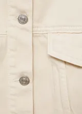 Chaqueta color crema estilo tejana vaquera, de corte oversize, con cuello camisero, cierre frontal de botones, mangas largas con puños abotonados, dos bolsillos de parche con solapa en el pecho y bolsillos laterales.