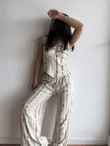 Conjunto de dos piezas, top halter con escote pronunciado y pantalón ancho de tiro alto con elástico, ambos con estampado vertical tipo tie-dye en tonos marrón sobre fondo beige claro.