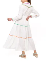 Vestido camisero largo de lino blanco con cuello camisero, cierre frontal con botones y cinturón de lazo. Presenta detalles de bordado ondulado en verde, naranja y rosa en cuello, bolsillos, puños y ruedo.