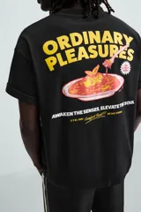 Camiseta negra de corte relajado, cuello redondo y manga corta. Presenta estampado frontal con la frase "Comfort Food!!! Our Daily Specials" y un dibujo de una flor.