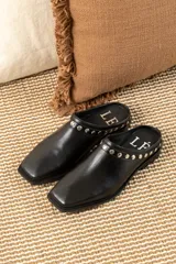 Mules de cuero negro con punta cuadrada y detalle de tachas plateadas en el borde superior.
