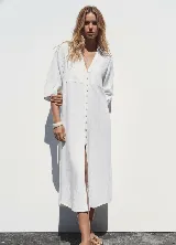 Vestido camisero blanco confeccionado en lino, de corte recto y largo midi. Presenta cuello camisero, mangas 3/4 con puños abotonados, cierre frontal con botones y abertura en el ruedo.