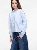 Camisa celeste cropped con tachas en el cuello y puños, con botones en la parte delantera y en los bolsillos. Tiene pinza en la parte trasera.