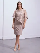 Vestido de fiesta color beige, de corte recto y largo a la rodilla, confeccionado en seda fría. Presenta una sobrecapa de microtul bordado con motivos florales.