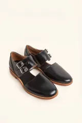 Zapato tipo monk strap con aberturas laterales, confeccionado en cuero vacuno color bordó. Presenta doble tira con hebillas metálicas plateadas en el empeine y suela de cuero con taco bajo.