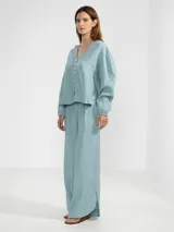 Camisa de lino color blanco, con cuello en V, manga larga con puños elásticos, cierre frontal con botones y dobladillo curvado.