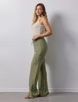 Pantalón verde oliva de rayón con cintura elastizada tipo smock y bordados florales en los bajos.