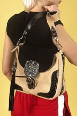 Bandolera de cuero texturado color beige con detalles en cuero croco negro y gamuza negra. Tiene correa regulable bicolor, flecos laterales, solapa con broche imán y bolsillo frontal con hebilla decorativa.