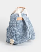 Mochila de denim azul con estampado paisley blanco, bolsillo frontal con cierre, correas regulables y manijas superiores de algodón con broche de cuerina. Acceso mediante cierre superior y puller de cuerina. Incluye tag de cuerina.