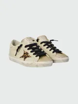 Zapatillas Golden Goose modelo Super Star, color crema con puntera dorada brillante, estrella de animal print y cordones negros.
