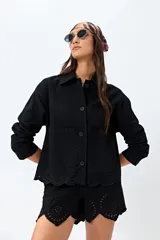 Sobrecamisa negra de algodón con botones frontales, cuello camisero y bolsillos de parche en el pecho. El ruedo inferior presenta un detalle de bordado calado (broderie) con terminación festoneada.