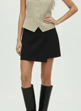 Pollera short de color negro con diseño cruzado en el frente y cierre lateral. Confeccionada en tejido de punto elástico suave con poliéster reciclado.