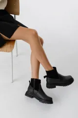 Bota de caña media color negro, con hebilla lateral y suela track.