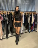 Top negro con escote halter que se ata en la nuca y la espalda, con detalle de nudo en la parte baja de la espalda. La prenda tiene un tejido con textura de terciopelo o jacquard con diseño de arabescos.