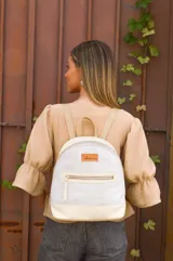 Mochila pequeña de cuero color gris claro y beige, con cierre superior y bolsillo frontal con cierre. Tiene asa de mano y correas ajustables para los hombros.