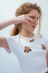 Remera blanca de corte cropped, con cuello redondo y mangas cortas. Presenta tres bordados de flores en el frente.