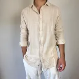 Camisa de lino color beige, de corte oversize, con cuello clásico y mangas largas con puños abotonados.
