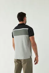 Remera tipo polo de manga corta con diseño a bloques de color: negro en cuello y mangas, gris oscuro en la parte superior del pecho, blanco en el centro y gris claro en el resto del cuerpo.