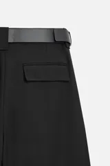 Pantalón negro de corte recto con cinturón de cuero sintético, pliegues frontales, bolsillos laterales y traseros con solapa.