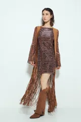 Chaleco largo color beige claro, estilo chaleco de gamuza, con apliques metálicos circulares perforados y largos flecos en el ruedo.