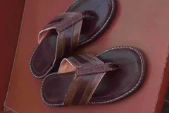 Chanclas de cuero color marrón oscuro con tiras anchas que presentan textura de piel de serpiente en tonos marrones y verdes. La suela es gruesa y está cosida a mano con hilo blanco contrastante.