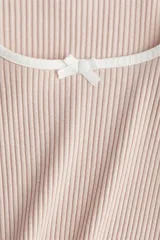 Top corto entallado de punto acanalado color rosa pálido, con mangas trompeta largas, escote cuadrado pronunciado con ribete fino blanco y moña de satén blanca. Ribetes sobrehilados en puños y bajo.