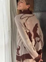 Campera de punto color beige con cuello polo y cierre frontal, puños en marrón y dibujo de un jinete en pleno rodeo en la espalda.