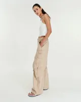 Pantalón cargo de gabardina gastada de lino y algodón color azul. Silueta de pierna recta ancha, con cartera con cierre metálico y broche níquel en el cruce de la cintura. Tiene bolsillos inclinados en los laterales y bolsillos cargo con tapa y broches metálicos a la altura de las rodillas, de los cuales salen unas tiras que se ajustan mediante hebillas metálicas para modificar la silueta del pantalón. En la espalda tiene pinzas y un bolsillo plaque con cierre metálico en boca. Es tiro medio.