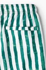 Short de baño blanco con rayas verticales verdes, cintura elástica con cordón ajustable, bolsillos laterales y bolsillo trasero con cierre autoadherente.