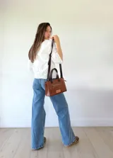 Cartera bandolera de cuero color marrón tostado, con doble asa corta y correa larga desmontable. Tiene un bolsillo frontal con cierre y un bolsillo interno.