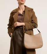 Bolso hobo mediano color beige, con asa corta al hombro y asa larga desmontable. Cierre superior con cremallera y detalles laterales contrastantes.
