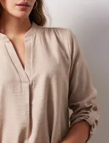 Blusa color beige de poliéster con escote en V y mangas 3/4 regulables con presilla y botón.