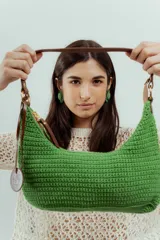 Cartera de hombro tejida a crochet color verde, con asa de cuero marrón y cierre.