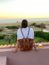 Mochila de cuero marrón con cierre superior y múltiples bolsillos externos. Se puede convertir en bolso de mano o bandolera gracias a sus correas ajustables y extraíbles.