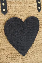 Bolso grande tipo tote de raffia color beige con aplique de corazón negro. Asas de mano y ribetes de cuero sintético negro.