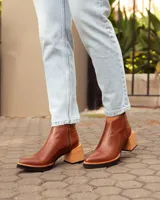 Botas de cuero color marrón, hechas a mano, con punta en pico y taco de madera cuadrado. Cierre lateral con cremallera.