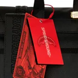Mochila negra con detalles en marrón y rojo, con estampado a cuadros en los bolsillos laterales y correas frontales.