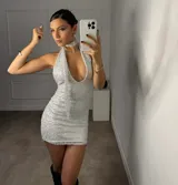 Vestido corto ajustado plateado con textura de lentejuelas o tejido brillante. Diseño halter con escote profundo en V y lazo que cae por el frente. Incluye un choker a juego.