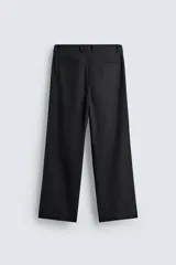 Pantalón de vestir negro, corte amplio, con pliegues en la cintura, bolsillos laterales y traseros de ojal.