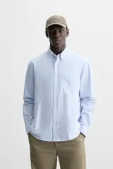 Camisa azul marino de corte regular fit, confeccionada en tejido de algodón Oxford. Tiene cuello abotonado, manga larga con puños abotonados, bolsillo de parche en el pecho y cierre frontal con botones.