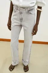 Jeans de tiro alto color negro lavado, con cintura cruzada, cinco bolsillos y pernera recta. El bajo está acabado en vuelta y tiene cierre frontal cruzado con cremallera y botones.