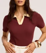 Blusa blanca acanalada de rib con cuello polo negro contrastante y mangas cortas.