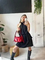 Minivestido negro con escote halter con detalle de flor, corte escalonado y falda corta.