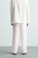 Pantalón blanco de lino con corte relajado (relaxed fit), cintura elástica, bolsillos frontales y un bolsillo trasero de vivo.
