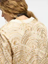 Camisa con estampado geométrico en tonos dorados y negros, con cuello mao y mangas largas acampanadas. Presenta cierre frontal con botones y lazos para atar en la cintura.